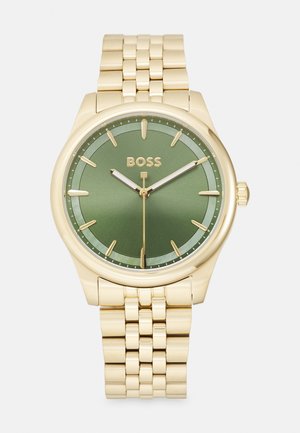 Montre-bracelet en or avec un cadran vert, présentant des index horaires, des aiguilles des heures et des minutes, et un bracelet en métal texturé.