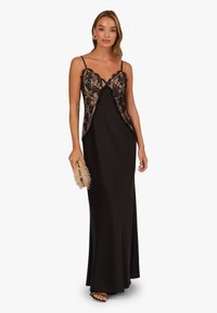 Abito nero con sovrapposizione in pizzo sul corpetto, spalline sottili regolabili e silhouette fluida. Tessuto dalla texture liscia.