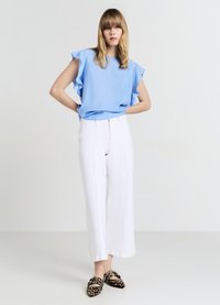 Haut bleu clair à manches courtes avec volants, associé à un pantalon blanc taille haute à jambes larges et des chaussures slip-on léopard noir et marron.