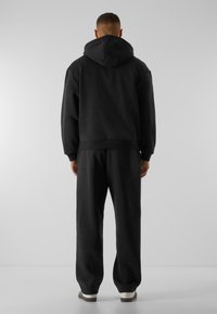 Haut à capuche noir, coupe décontractée, avec des poignets côtelés, associé à un pantalon de jogging noir assorti. Tissu doux et design minimal.