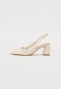 Beige skinnslingback-sko med spiss tå, lav blokkheel og liten bue-detail foran. Glatt tekstur og minimalistisk design.