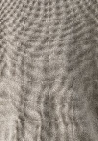 Sweter o strukturze waflowej w jasnym kolorze taupe, z teksturowaną powierzchnią, zapewniający komfortowy wygląd i luźny krój.