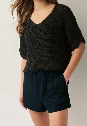 Crochet black pullover with a V-neck and rolled short sleeves paired with navy blue drawstring shorts. Soft, textured fabric.