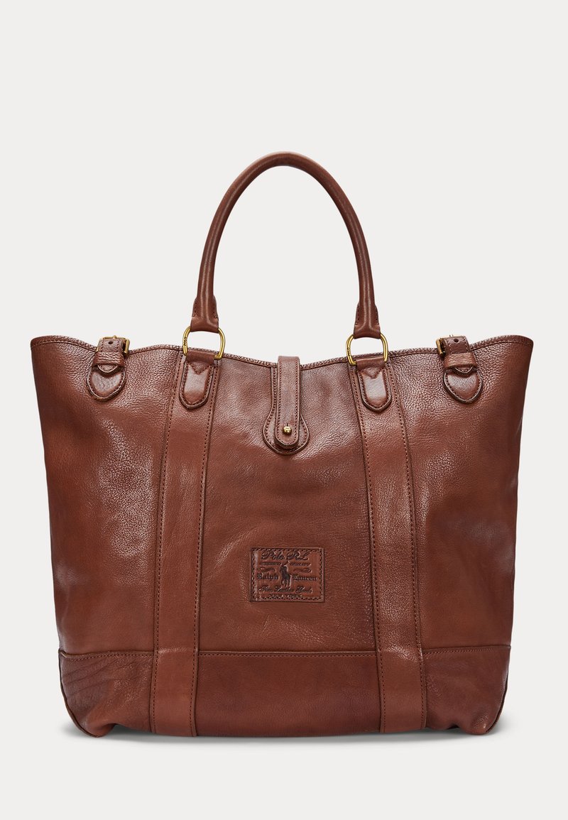 Sac cabas en cuir marron avec double anses, détails de boucles couleur or, et une étiquette logo cousue au centre avant.