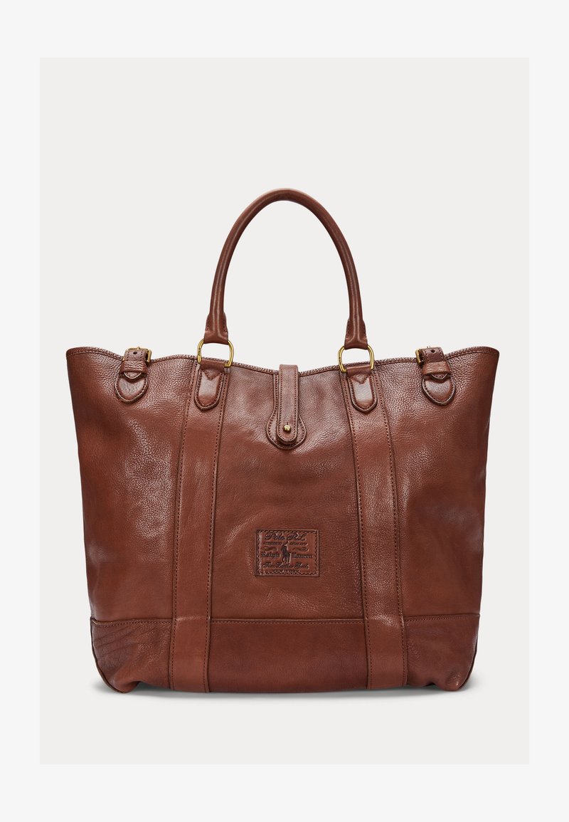 Sac cabas en cuir marron avec double anses, détails de boucles couleur or, et une étiquette logo cousue au centre avant.
