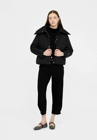 Must pehmevoodriga jakk kõrge krae, trukkidega ja laatri lõikega. Kandmisparina mustade pükste ja madalate jalanõudega. Pind ühtlaselt sile.