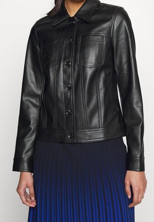 Kobieta ubrana w dopasowaną czarną skórzaną kurtkę z przodu zapinaną na guziki i z kieszeniami na piersiach, w połączeniu z niebieską plisowaną spódnicą.