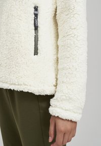 Witte fleece pullover met een gestructureerd oppervlak, een zwarte ritszak met een merk pull tab en een omgeslagen zoom.