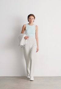 Ανοιχτό μπλε τοπ, λευκά φόρμα και λευκά αθλητικά παπούτσια. Το μοντέλο κρατάει ένα λευκό μπουφάν. Απλή σχεδίαση, μαλακή υφή και ελάχιστες λεπτομέρειες.