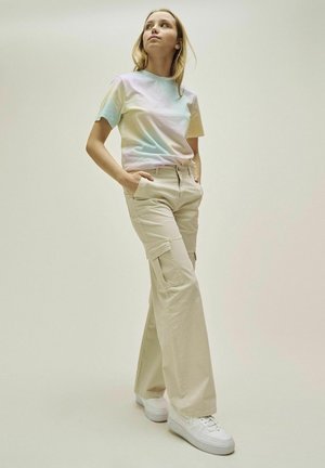 Pastel gradient kortærmet t-shirt parret med beige cargo-bukser med lommer, båret med hvide sneakers på en neutral baggrund.