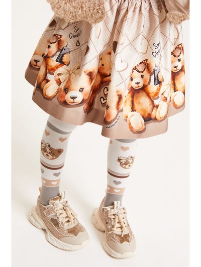 Jupe beige à motif ours, ornée d'un imprimé vichy, associée à des chaussettes grises avec des designs d'ours et des chaussures de sport beige clair.