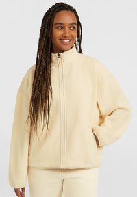 Giacca in pile di colore crema con colletto alto, zip completa e tasche laterali. Tessuto morbido con una vestibilità comoda e minimalismi nel branding.