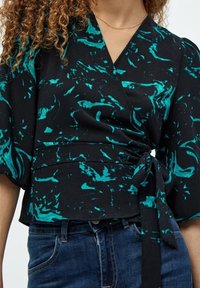 Must mustriga tipp musta värviga, teal'i abstraktse mustriga, lühikeste puffvarrukatega ja seotud vööga. Kandmiseks sinised denim teksad.