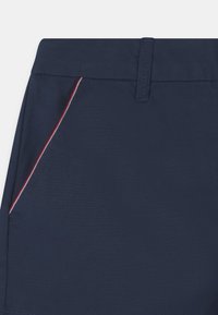 Pantaloni corti blu navy realizzati in tessuto liscio, con vita piatta e una tasca laterale con dettagli di cucitura rossa e bianca.