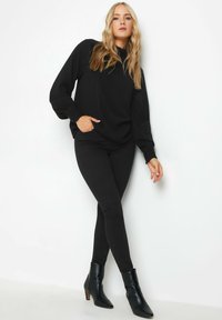 Maglietta nera a maniche lunghe con spalle arricciate, abbinata a pantaloni neri attillati e stivali neri alla caviglia con punta e tacco appuntiti.