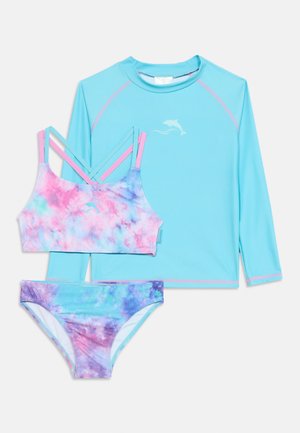 T-shirt de bain à manches longues bleu clair avec logo dauphin, associé à un haut de bikini tie-dye rose, bleu et violet et un bas assorti.