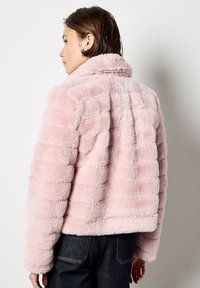 Giacca in pelliccia sintetica rosa con strisce orizzontali, colletto alto e design cropped. Tessuto morbido e vestibilità rilassata, mostrata da dietro.