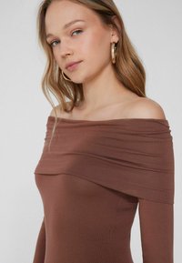 Braunes Off-Shoulder-Top mit figurbetontem Design, weichem Material und geschichtetem Stoff am Ausschnitt, ausgestattet mit einer glatten Oberfläche.