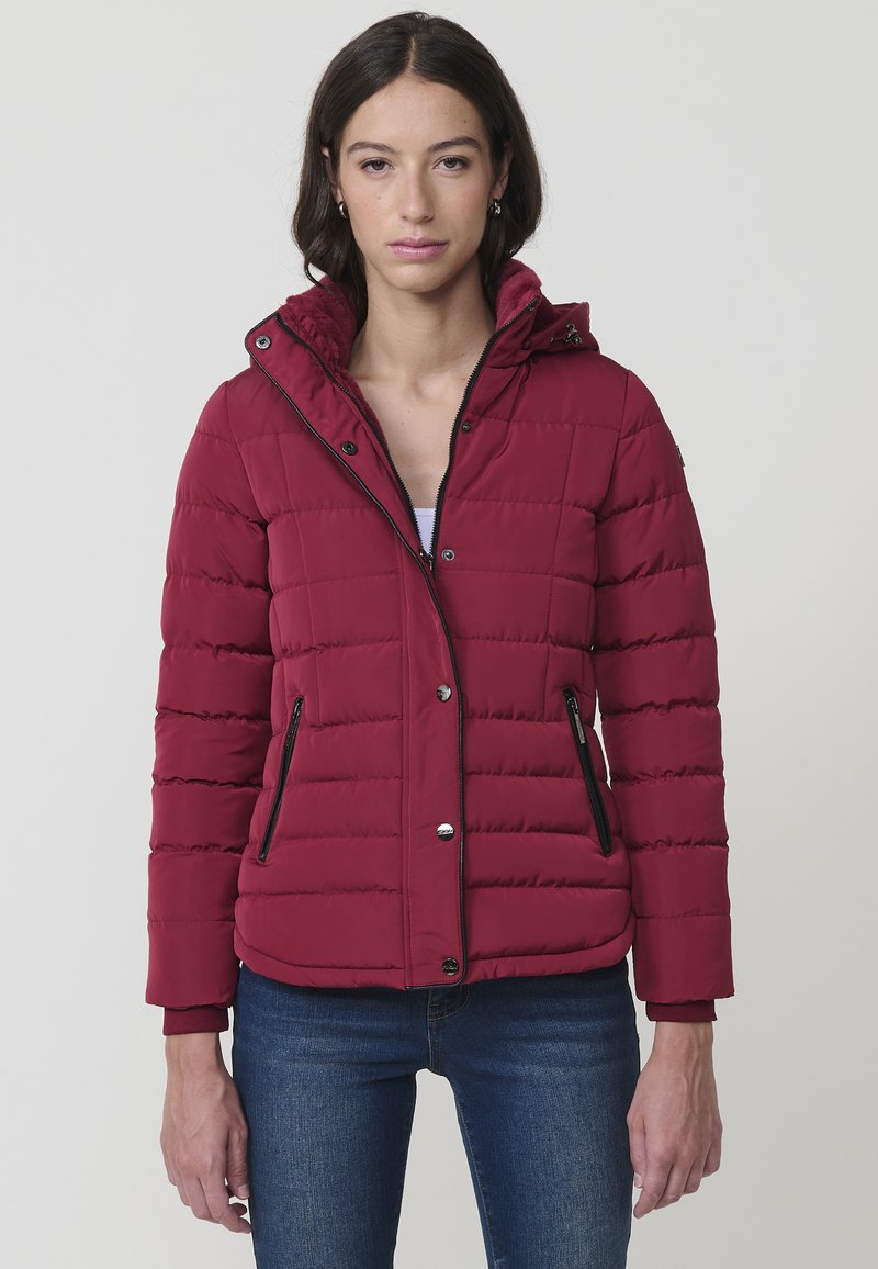 Burgundijas pūkains mēteļ-jaka ar kapuci, quilted tekstūra, ar rāvējslēdzēja kabatām un melna rāvējslēdzēja detaļām. Piemērots ir nedaudz apgriezts, veidots ar zilām biksēm.