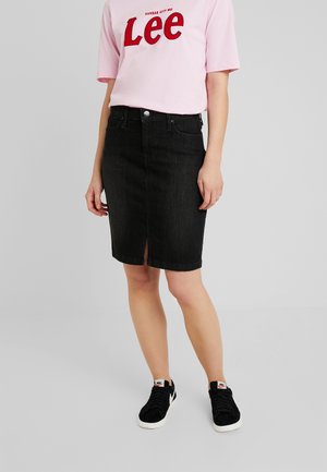 Falda de lápiz de mezclilla negra con una abertura frontal, combinada con una camiseta rosa que muestra "Lee" en letras rojas en negrita y zapatillas negras.