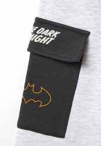Tela gris con un detalle de mangas gris oscuro presenta el texto "EL CABALLERO OSCURO" y un logo de Batman en color naranja. Material suave y texturizado.