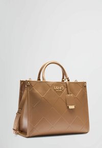 Borsa a tracolla di colore tan realizzata in ecopelle trapuntata, caratterizzata da un logo dorato, doppi manici e una tracolla regolabile. Texture liscia con una forma strutturata.