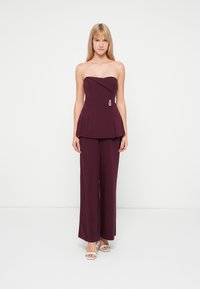 Top peplum bordeaux sem alças com decote curvo, combinado com calças de perna larga. Detalhe notável em dourado na cintura.