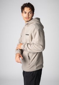Hellbeiges Kapuzensweatshirt aus weichem Stoff mit einer vorderen Reißverschlusstasche. Mit schwarzem "WORLDWIDE"-Schriftzug auf der Brust und gerippten Bündchen.