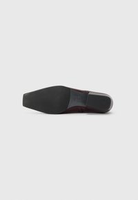 Semelle de chaussure en caoutchouc noir à texture lisse. La tige est en cuir bordeaux, avec des détails de couture subtils et une forme de pointe.