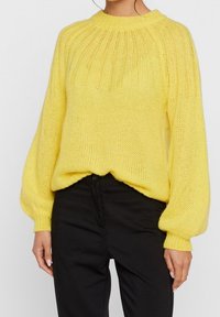 Yellow knitted sweater with a ribbed design, round neckline, and voluminous long sleeves, paired with black trousers.