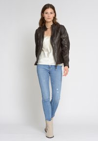 Brun läderbikerjacka med dragkedja framtill, texturerad yta och figurnära design. Matchad med ljusblå slitna jeans och beige ankelstövlar.