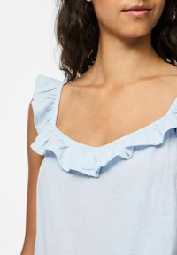 Ljusblå linne i mjukt tyg med fyrkantig halsringning och volangdetaljer runt axelbanden.