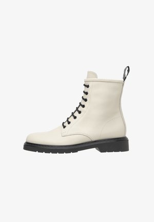 Hvide læder ankelstøvler med sorte snørebånd, rund tå og en struktureret sort gummisål. Har en løkke bagpå for nem påtagning.