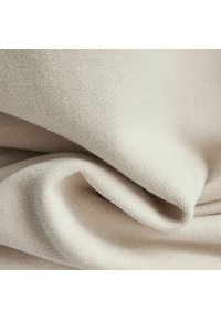 Tessuto a maglia beige chiaro con una texture morbida, piegato per mostrare una trama liscia e uniforme e sottili variazioni di tonalità.