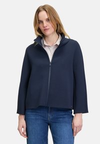 Navyblaues Zip-Jackett mit hohem Kragen, aus weichem Stoff. Hat eine lockere Passform und einen leichten Schnitt am Saum, der gut zu blauen Jeans passt.