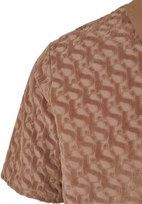 Tissu marron à manches courtes avec un motif géométrique en relief et texturé et un col à côtes.