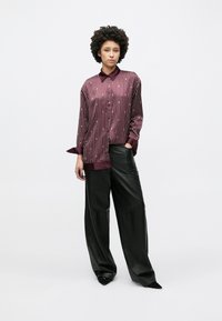 Burgundská košile s dlouhým rukávem s vertikálními pruhy, zapínáním na knoflíky vpředu a kontrastními manžetami, doplněná černými koženými kalhotami s širokými nohavicemi.