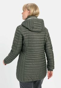 Gevoerde groene jas met een capuchon, voorzien van een gewatteerd ontwerp en geribde manchetten, gemaakt van een lichtgewicht materiaal met een zachte textuur.
