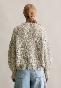 Gruby sweter w jasnoszarym i kremowym kolorze, z rękawami typu raglan, ribbowym wykończeniem i teksturowanym materiałem. Połączony z jeansami z wysokim stanem.