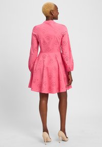 Rotes Kleid mit langen Ärmeln, gewelltem Saum und floralen Ausschnitten. Tailliert und mit einem ausgehenden Rock; kombiniert mit nudefarbenen Absatzschuhen.