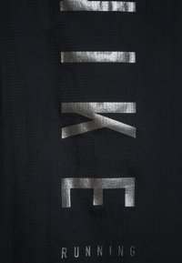 Czarna tkanina sportowa z dużym, metallicznym srebrnym napisem "NIKE" oraz tekstem "RUNNING" poniżej w boldzowej, nowoczesnej czcionce. Teksturowana powierzchnia.