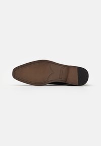 Semelle de chaussure marron avec une finition en cuir lisse, une bande de roulement à motifs, un détail de couture latérale et un accent surélevé près du talon.