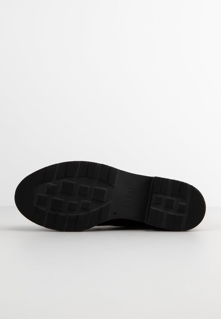 Suola delle scarpe in gomma nera con superficie testurizzata, caratterizzata da un motivo a coste per migliorare la presa e una punta arrotondata. Logo impresso nella zona del tallone.