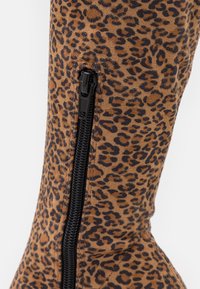 Primer plano de tela con estampado de leopardo y una cremallera negra vertical parcialmente cerrada sobre una superficie curva.