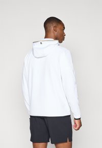 Weißer Kapuzenpullover mit kontrastierendem schwarzen Saum und Kragen. Glatte Textur und minimalistisches Design. Rückansicht, gezeigt mit Shorts.