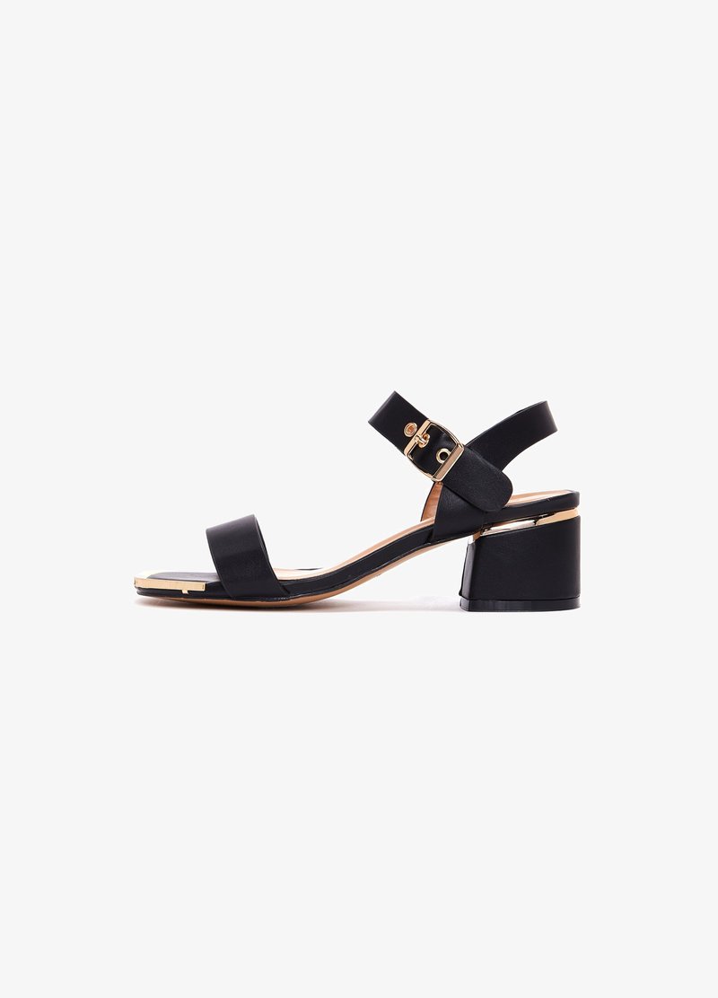 Sandale en cuir noir avec un bout arrondi, deux larges brides et une boucle dorée. Caractéristiques d'un talon épais et d'une texture lisse.