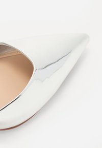 Bílé lakované kožené lodičky s špičatou špičkou a elegantním designem, s výřezem v přední části a hladkým, reflexním povrchem.