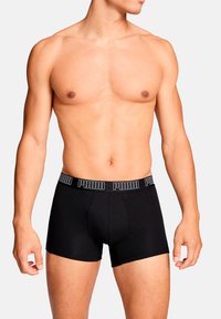 Schwarze Boxer-Shorts mit eng anliegendem Schnitt, aus weichem Stoff gefertigt. Mit einem elastischen Bund mit Markenlogo "PUMA" in kontrastierenden Farben.