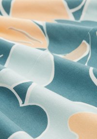 Weicher Stoff mit einem abstrakten Blumenmuster in Teal, Beige und Hellblau, dargestellt mit sanften Falten und Knicken.