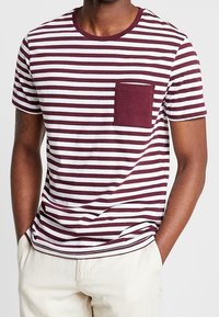 Camiseta de manga corta con rayas burdeos y blancas, con cuello redondo y un bolsillo en el pecho, confeccionada en una tela suave.